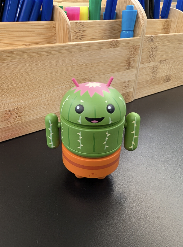 一个绿色的小 Android 机器人，外形像仙人掌，坐在黑色表面上。
